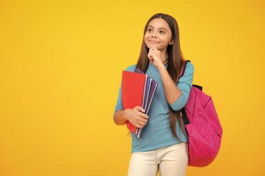 Schoolchild, teenage student girl hold book on yellow isolated studio background. School and education concept. Back to school. Thinking face, thoughtful emotions of teenager girl