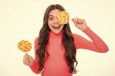 Şekerli lolipop yiyen genç bir kız. Çocuklar için şeker ve şeker. Çocuk beyaz izole arka planda lolipop yiyor. Lezzetli karamel, şekerci dükkanı. Heyecanlı bir yüz, neşeli genç bir kız.