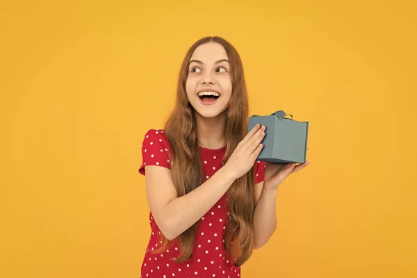 Excited face, cheerful emotions of teenager girl. Child teen girl 12-14 years old with gift on yellow isolated background. Birthday party, holiday present concept