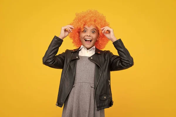 Girl with yellow wig. Funny child wearing orange curly wig hair, summer fun. Excited face, cheerful emotions of teenager girl