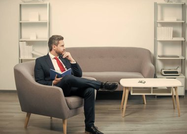 Takım elbiseli olgun bir işadamı ofiste oturup not defterine not alır. karar vermek.