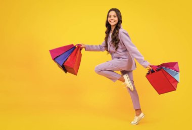 Child girl hold shopping bag enjoying sale isolated on yellow background. Run and jump. Portrait of teenager girl is ready to go shopping
