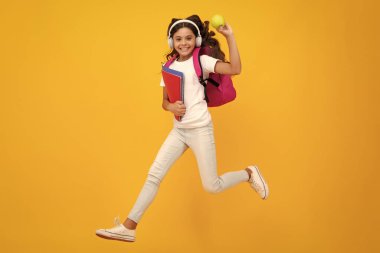 Okul çocuğu, kulaklıkları ve sarı izole stüdyo geçmişine sahip okul çantalı genç kız. Çocuk okulu ve eğitim konsepti
