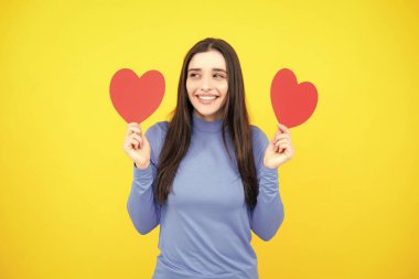 Mutlu kadınlar, sevgililer günü ya da doğum günü için aşk sembolleri. Ellerinde kalbi olan güzel genç bir kadın. Sarı arka planda kağıt kalpli çekici bir kadın.