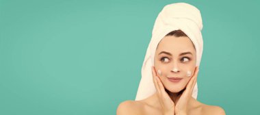 cheerful young lady apply face cream on blue background. Beautiful woman isolated face portrait, banner with mock up copy space