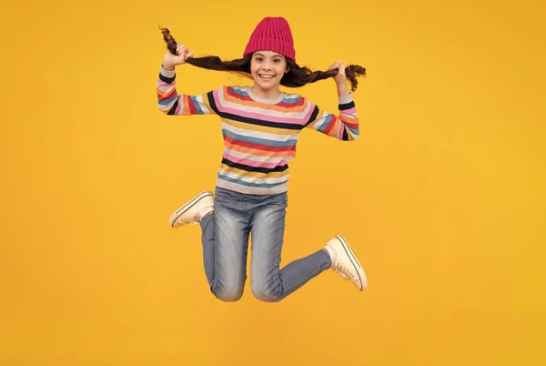 Amazed teenager. Teenager girl with winter hat over isolated yellow background. Winter christmas holidays, new year mood. Jump and run. Kids warm clothes. Excited teen girl