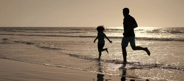 Silhouette of father and son run on summer beach outdoor, banner poster with copy space, father and son silhouettes running having fun and feel freedom on summer beach, summer vacation.