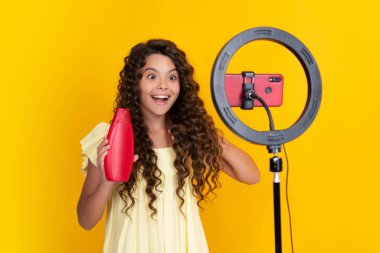 Child vlogger making video blog on phone. Teen girl blogger influencer recording video for social media, hold hair conditioner or shampoo bottle. Happy teenager, positive and smiling emotions of teen