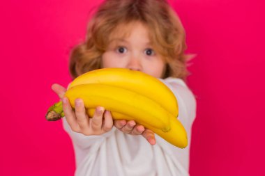 Child hold banana in studio. Studio portrait of cute kid boy with bananas isolated on red background