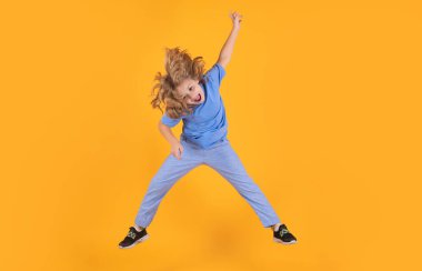 Funny boy jumping in air. Kid boy jump fly movement wear shirt and jeans isolated on yellow studio background