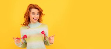 Woman isolated face portrait, banner with copy space. happy cheerful redhead girl with red heart sticks on yellow background. february 14