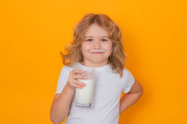 Little child drinking milk. Kid with glass of milk on yellow isolated background