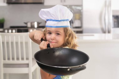 Aşçı çocuk aşçı. Yemek pişiren çocuklar. Önlüklü ve aşçı şapkalı çocuk mutfakta sağlıklı bir yemek hazırlıyor. Yemek pişirme süreci