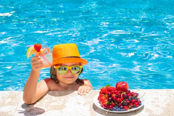 Little child by the pool eating fruit and drinking lemonade cocktail. Summer kids vacation concept