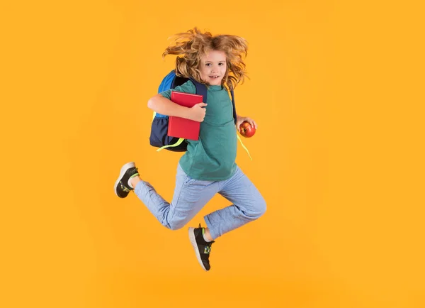 Full length body of little school kid jumping having fun isolated yellow color background. Crazy school boy jump