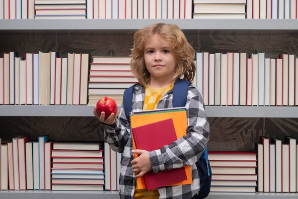 School boy with books and apple in library. Child from elementary school with book. Little student, clever nerd pupil ready to study. First time to school. Concept of education and learning