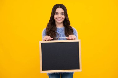 Okul satış kurulu. Neşeli genç kız, sarı arka planda fotokopi alanı olan karatahta tutuyor. Mutlu ergen, pozitif ve gülümseyen genç kız duyguları