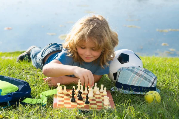 Chess school outdoor. Child think or plan about chess game, laying on grass in summer park. Intelligent, smart and clever school kids