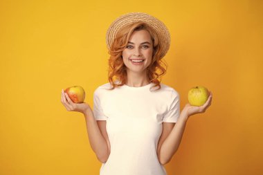 Sağlıklı dişleri olan, yaz hasır şapkalı, gülümseyen kızıl kadın elma tutuyor. Stüdyoda izole edilmiş