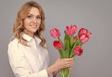 Gri arka planda bahar lale çiçekleri olan mutlu genç bir kadının yüzü.