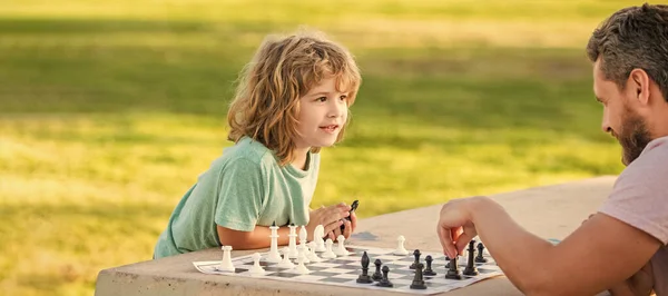 Father and son play chess outdoor, banner poster with copy space, happy family of dad and son boy playing chess on table in park outdoor, chess competition.