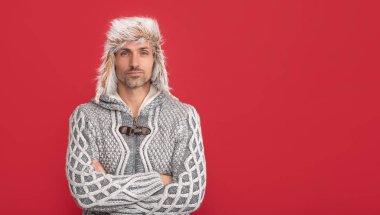 grizzled guy in sweater on red background. hoary man wear warm hat. male winter fashion. mens beauty. mature guy portrait. copy space. man in earflap hat.