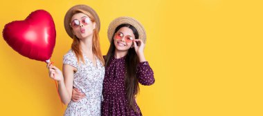 Mother and daughter kid banner, copy space, isolated background. happy mom and daughter hold love heart balloon on yellow background