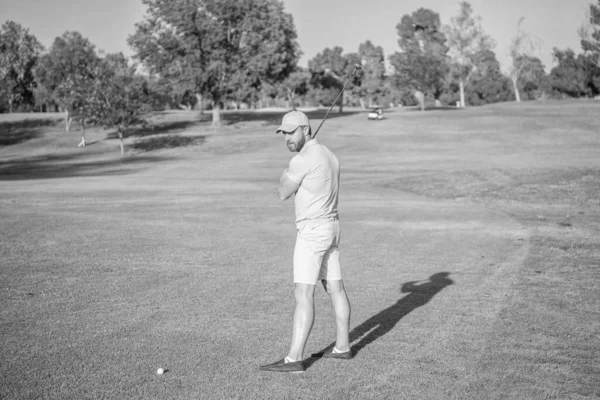 golfer in cap with golf club. people lifestyle. man playing game on green grass. summer activity. professional sport outdoor. full length. male golf player on professional golf course.