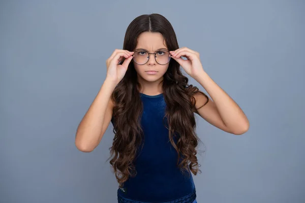 Serious teenager girl. Tennager child girl wear eyeglasses looking at camera with confidence over yellow background, copy space. Kid get eyesight
