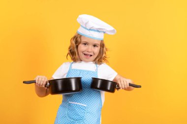 Kid chef cook with cooking pot stockpot. Kid in cooker uniform and chef hat preparing food on studio color background. Cooking, culinary and kids food concept