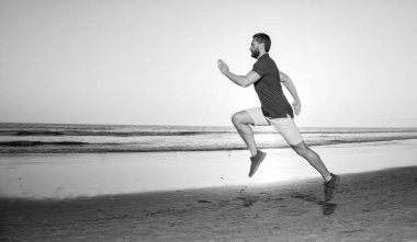 Spor koşucusu gün batımında koşuyor. Yaz plajı, taklit alanı, koşu..