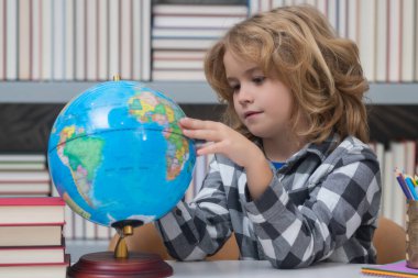 School pupil looking at globe in library, geography lesson. School child studying in classroom at elementary school. Kid studying on lesson in class at elementary school