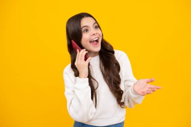 Heyecanlı ergen çocuk elinde cep telefonu tutuyor. Güzel bir genç kızın cep telefonu, cep telefonu uygulaması kullanarak yakın plan portresi, parlak sarı renkli arka planda izole edilmiş.