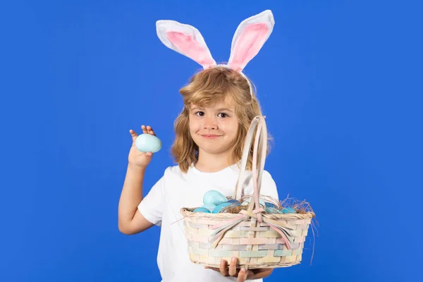 Cute little boy with bunny ears holding easter egg on color blue background. Kid boy with bunny ears hold easter basket with easter eggs