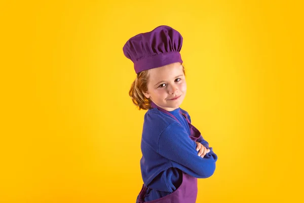 Kid in cooker uniform and chef hat preparing food on studio color background. Cooking, culinary and kids food concept