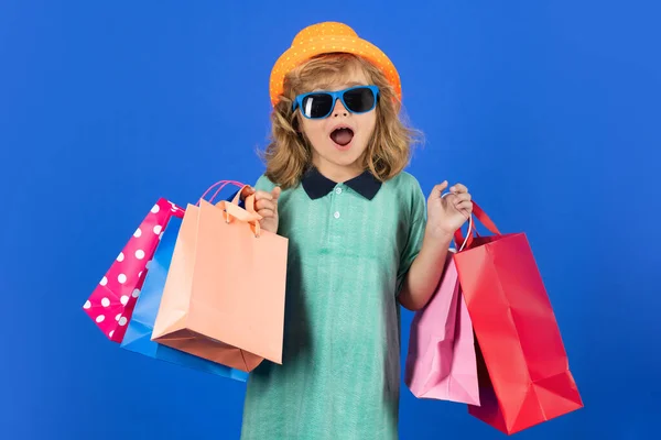 Kid boy in fashion clothes goes shopping. Kid with shopping packages. Shopper child with carrying shopping bags