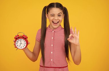 Child student girl with clock isolated on yellow background. Child back to school. Education and time concept. Happy teenager, positive and smiling emotions of teen girl