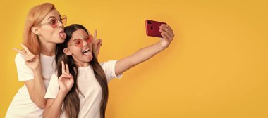 Anne ve kız çocuk afişi, kopyalama alanı, izole edilmiş arka plan. Mutlu anne ve çocuk akıllı telefondan selfie çekiyor. Barışı gösteriyor, blog yazarı.