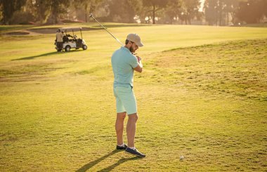 Yaz etkinliği. Profesyonel açık hava sporu. Profesyonel golf sahasında erkek golfçü. Golf sopasıyla şapkalı golfçünün portresi. İnsanların yaşam tarzı. Yeşil çimlerde oynayan atletik adam.