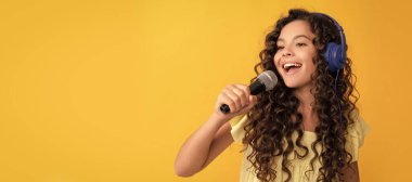 cheerful teen girl listen music in headphones and singing in microphone, vocal school. Child portrait with headphones, horizontal poster. Girl listening to music, banner with copy space clipart