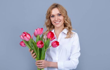 glad young woman with spring tulip bouquet on grey background.