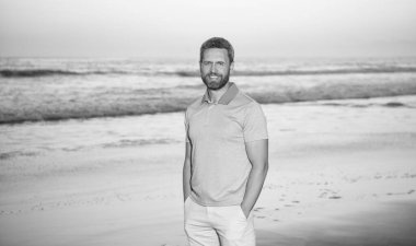 Gündoğumu plajındaki beyaz adam. Gömlekli sakallı adam. Yaz modası. Yaz tatili. pozitif duygular. Gün batımında sakallı gülümseyen bir adam. Sabah kumsalındaki traşsız adam..