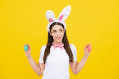 Happy Easter. Portrait of young smiling woman with bunny ears isolated on yellow studio background. Easter bunny woman looks fun. Easter eggs
