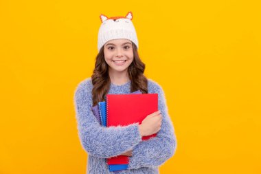 happy teen girl wear hat holding notebook on yellow background, homework.