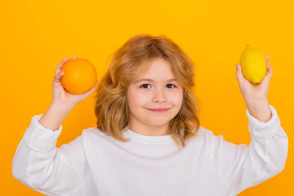 Kid with orange and lemon in studio. Studio portrait of cute child hold lemon and orange isolated on yellow background
