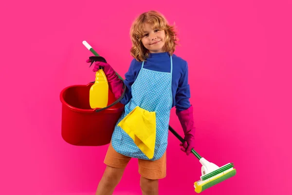Portrait of funny child cleaning. Housekeeping and home cleaning concept. Child use duster and gloves for cleaning. Studio isolated pink background