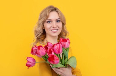 glad young woman with spring tulip flowers on yellow background.