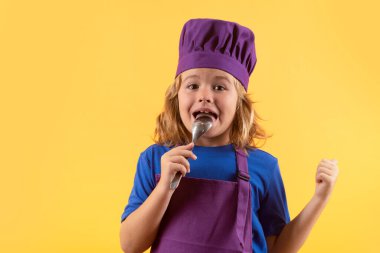 Funny kid chef cook with spoon, studio portrait. Cooking children. Chef kid boy making healthy food. Portrait of little child in chef hat isolated on studio background. Kid chef. Cooking process