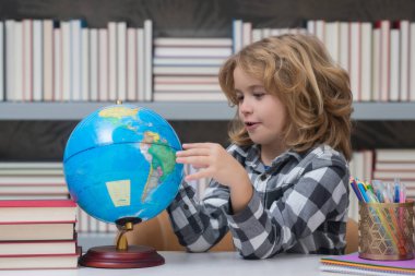 School kid pupil looking at globe in library at the elementary school. World globe. School child 7-8 years old with book go back to school. Little student