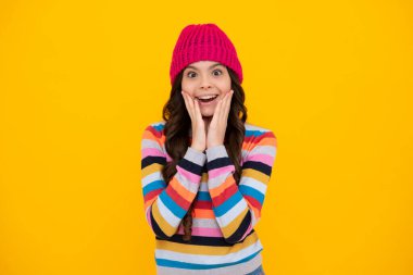 İzole edilmiş sarı arka planda kazak ve örgü şapka giyen modern bir genç kız. Mutlu ergen, pozitif ve gülümseyen genç kız duyguları